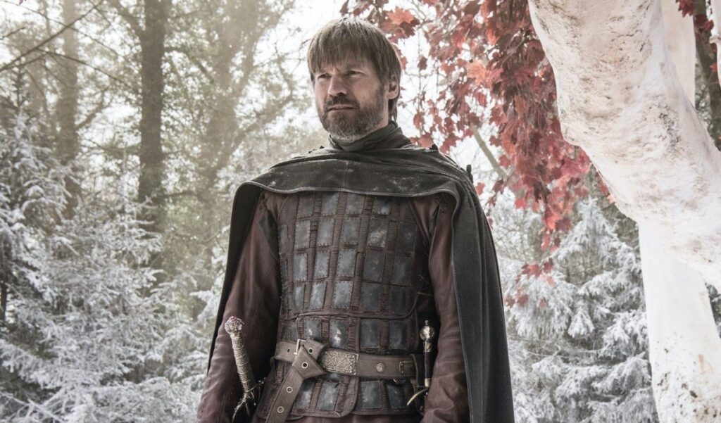A man in medieval armor stands in a snowy forest with red-leaved trees.