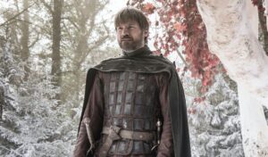 A man in medieval armor stands in a snowy forest with red-leaved trees.
