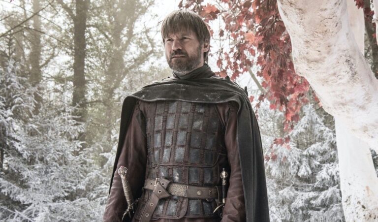 A man in medieval armor stands in a snowy forest with red-leaved trees.