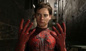 A man in a Spider-Man costume looks surprised with his hands raised in front of him, standing in a dimly lit alley.