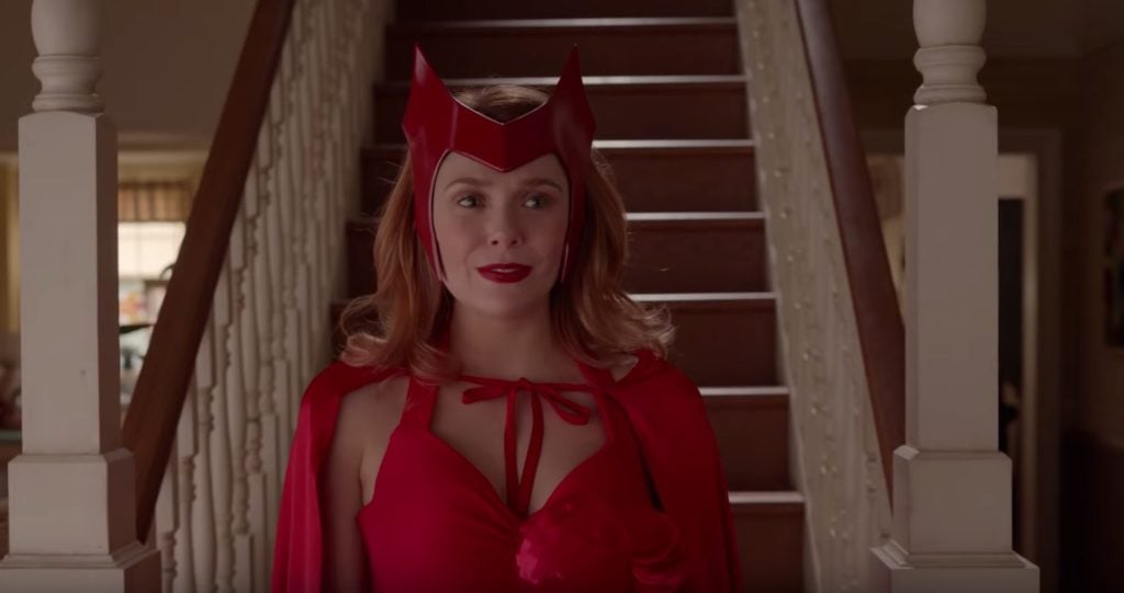 A woman in a red costume standing in front of stairs.