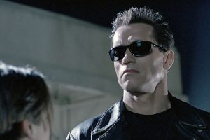 Man in sunglasses and leather jacket stares intently.