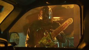 A man with bloody face holding a chainsaw.