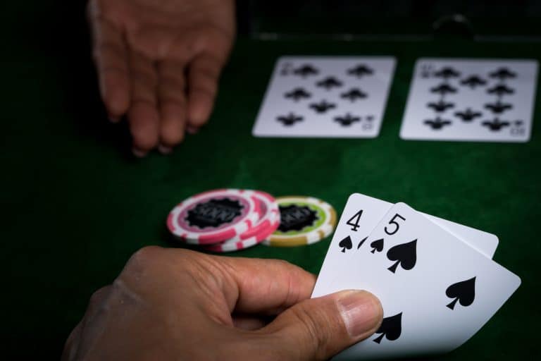 How Technology Has Changed The Way People Try Online Blackjack A hand holding a 4 and 5 of spades at a poker table, with poker chips and two face-up cards on the felt surface.