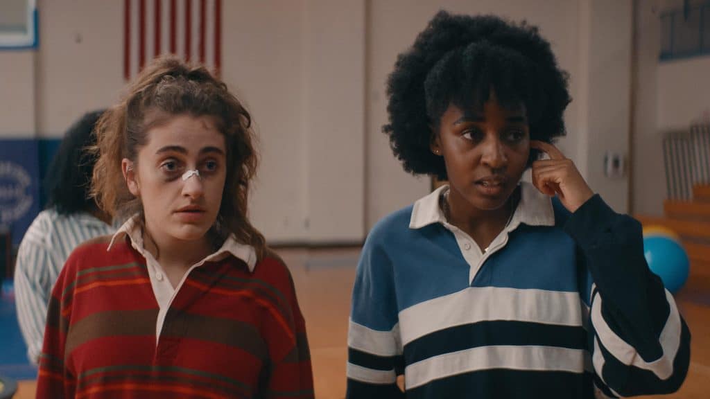 Two girls standing in a gym talking on their cell phones.