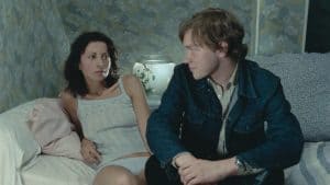 A man and a woman sitting on a bed.