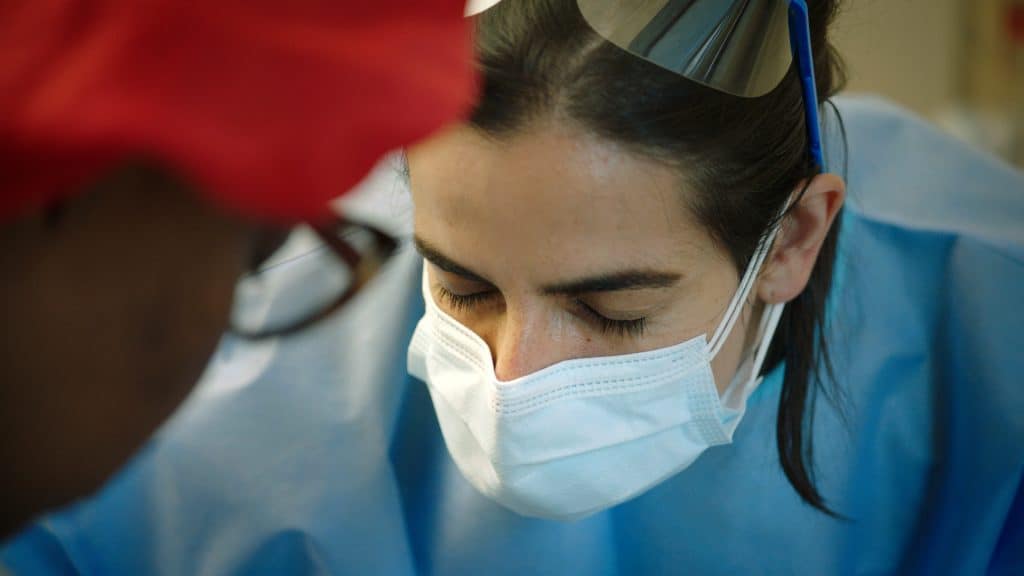 A woman wearing a surgical mask is looking at a patient.
