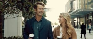 A man and woman are walking down the street holding coffee cups.