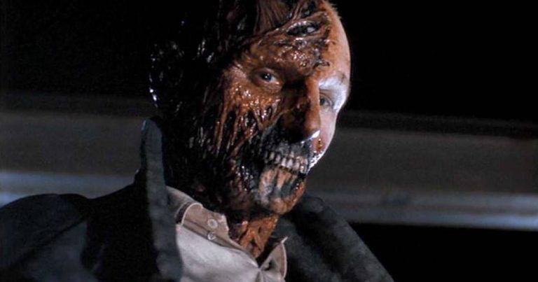 A man with a bloody face is standing in a dark room.