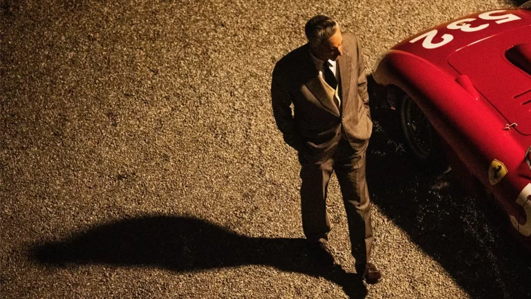 A man in a suit standing next to a red sports car.