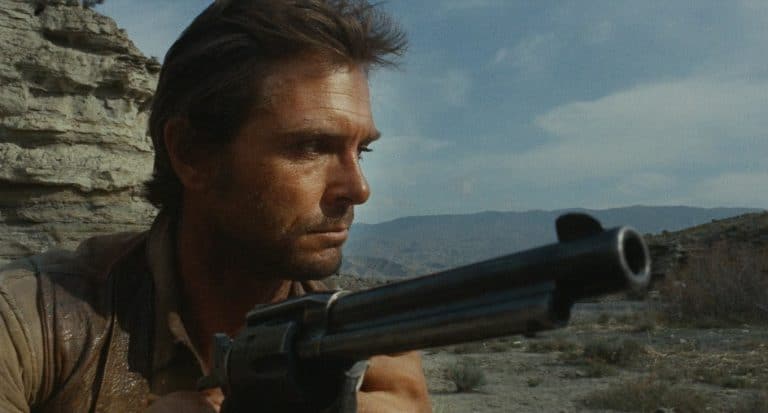 A man holding a gun in the desert.