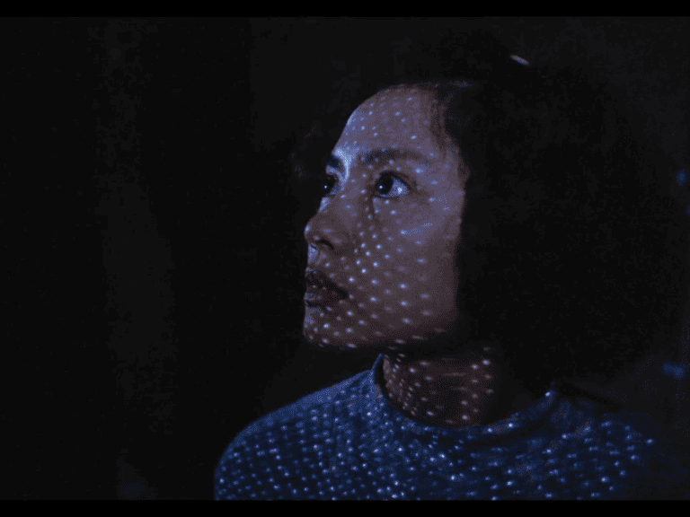 A woman in a dark room with dots on her face.