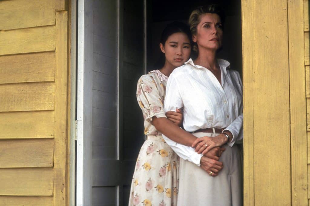 Two women standing in the window of a yellow house.