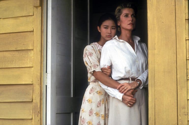 Two women standing in the window of a yellow house.
