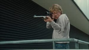 ‘I… For Icarus’ Blu-Ray Review – A Riveting Paranoid Thriller Not To Be Missed A man holding a gun on a railing.