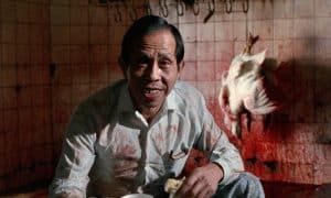 A man sitting in front of a bloody chicken.