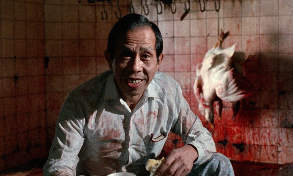 A man sitting in front of a bloody chicken.