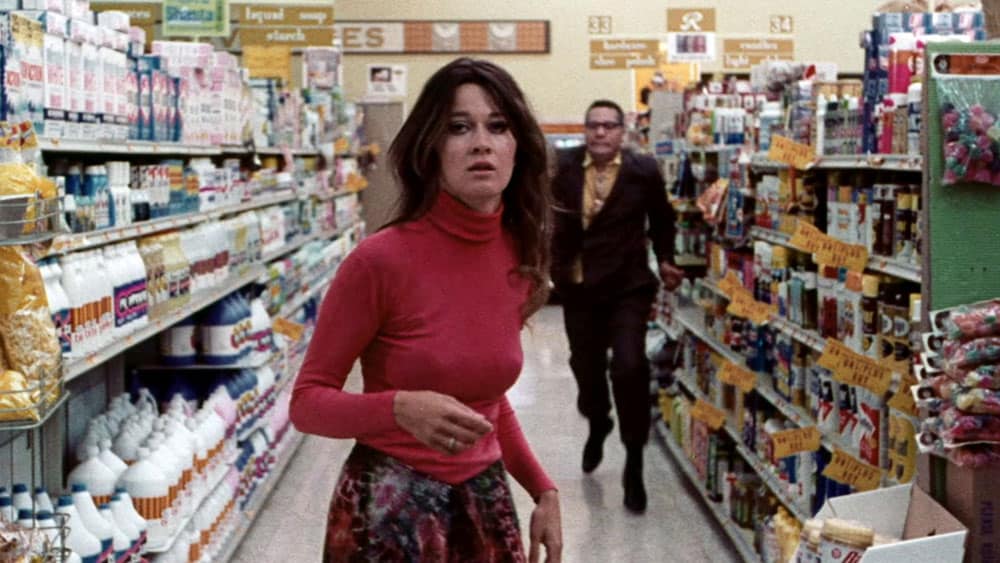 A woman walking down a aisle of a grocery store.
