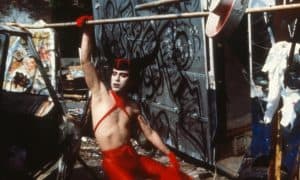 ‘Mondo New York’ Blu-Ray Review – An Ode To Misfits, Perverts, And Forgotten Artists A man in a red outfit holding a bat.