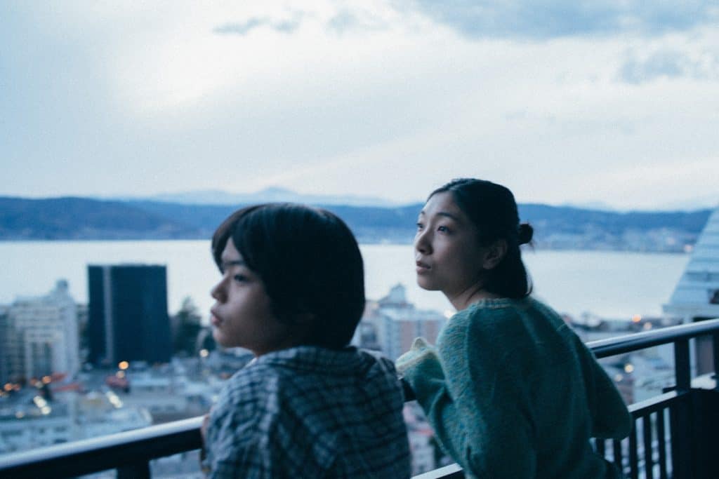 Two asian women standing on a balcony overlooking a city.