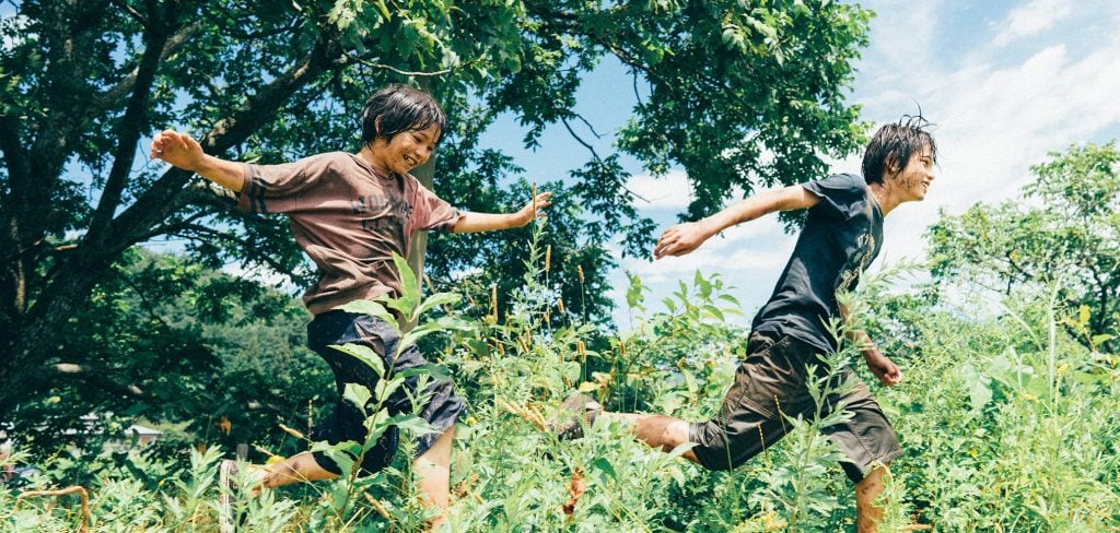 Two boys running through a field with a frisbee.