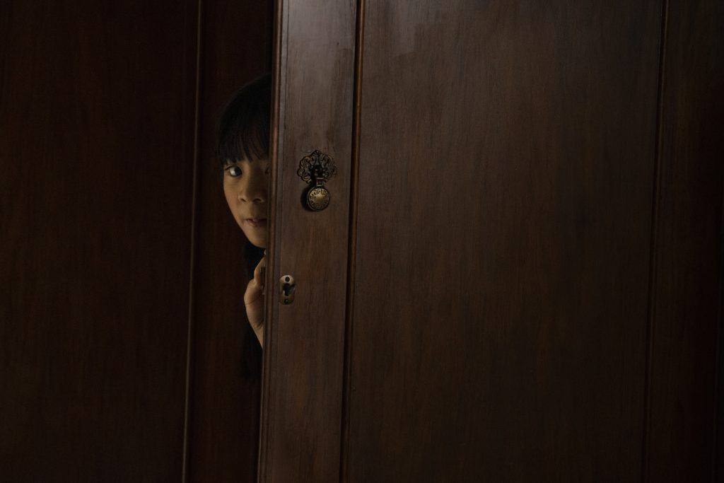 A girl peeking out of a wooden door.