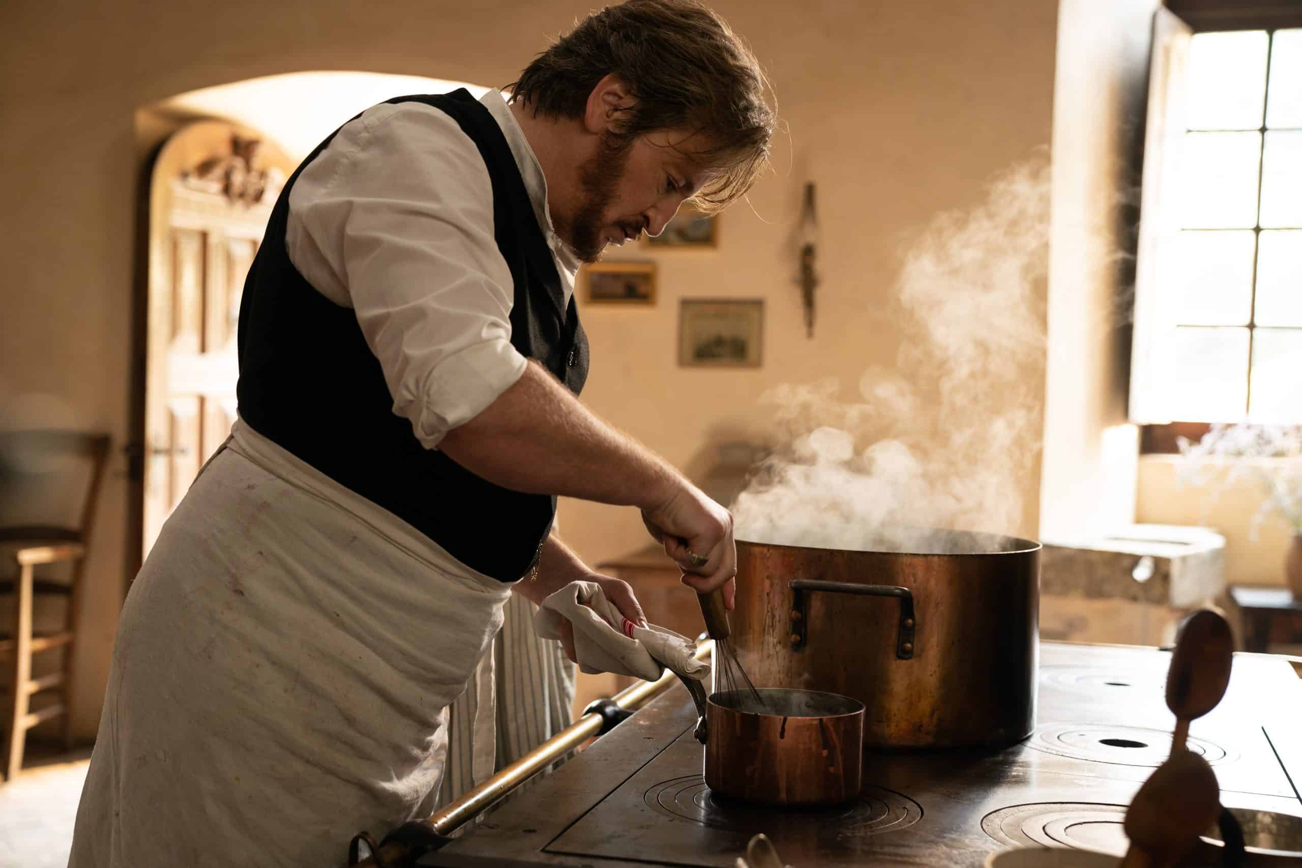 A man in an apron cooking in a kitchen.
