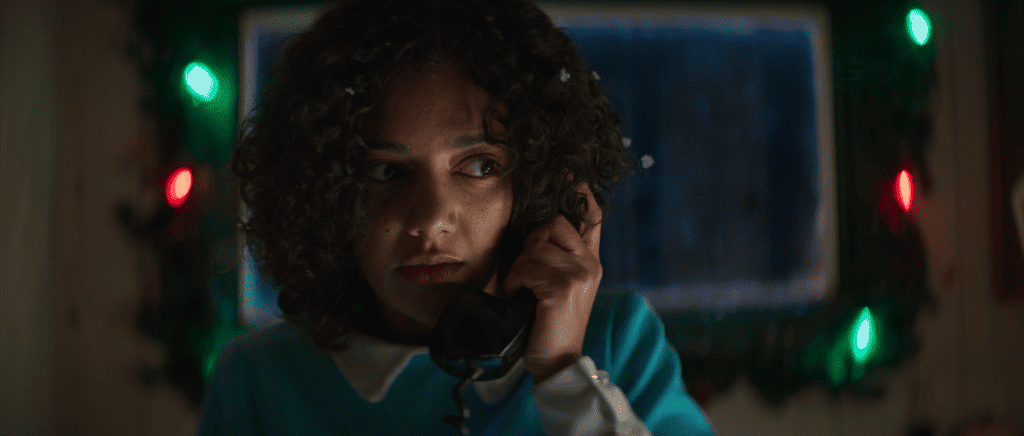 A girl talking on the phone in front of christmas lights.