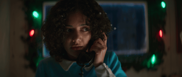 A girl talking on the phone in front of christmas lights.