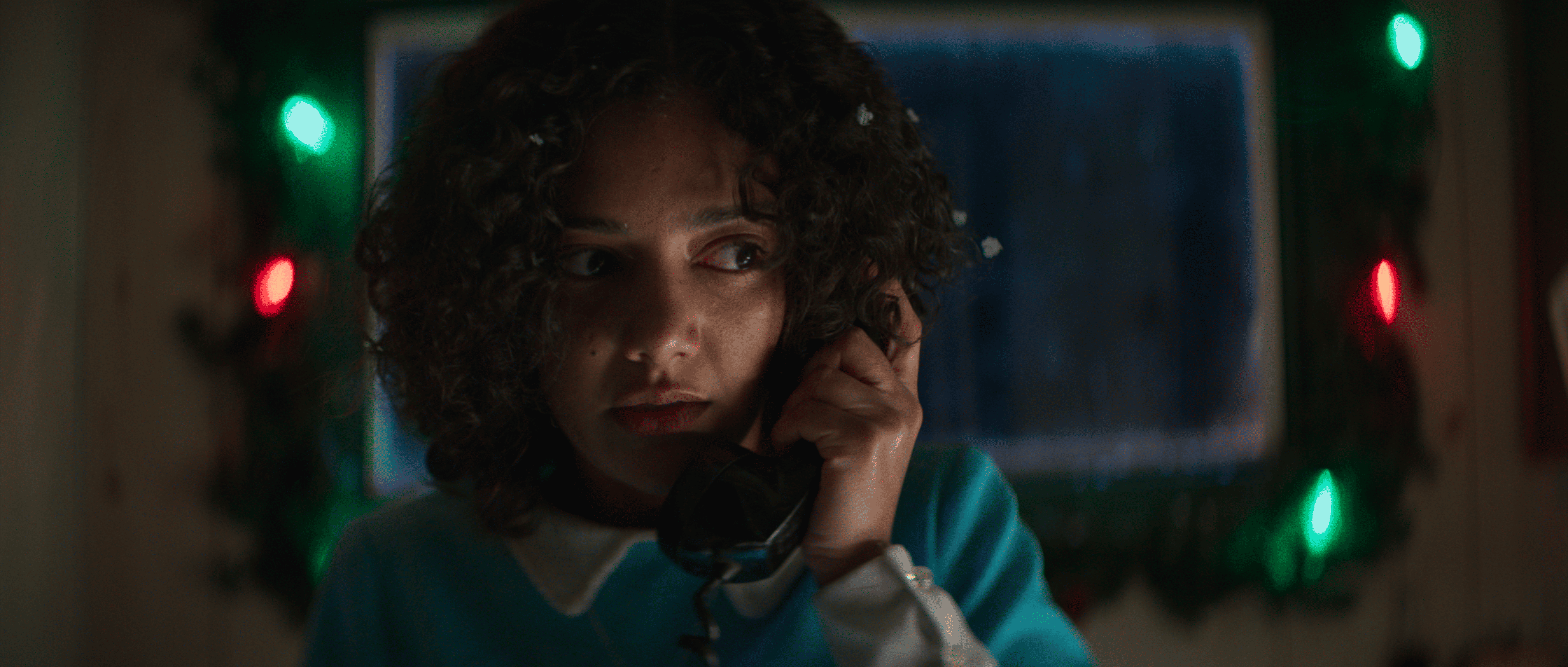A girl talking on the phone in front of christmas lights.