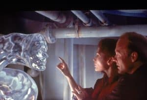 Five Iconic James Cameron Films Head To 4K UHD Blu-Ray Including ‘True Lies’ And ‘The Abyss’ A man and woman looking at a glass sculpture.