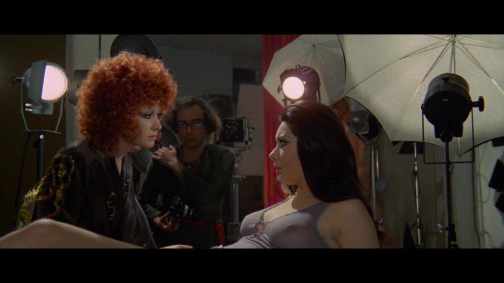 A woman with red hair is laying on a bed next to a camera.