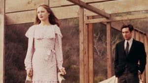 A man and woman in a pink dress standing next to a wooden structure.
