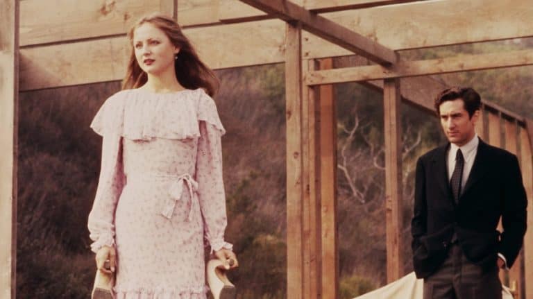 A man and woman in a pink dress standing next to a wooden structure.