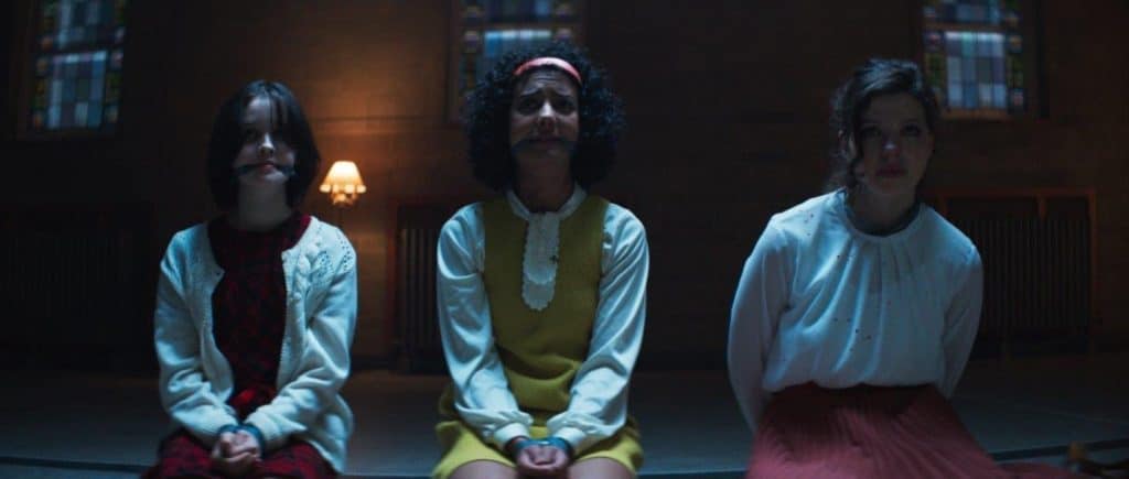 Three young girls sitting on the floor in front of a stained glass window.