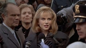 A woman in a suit is surrounded by reporters.