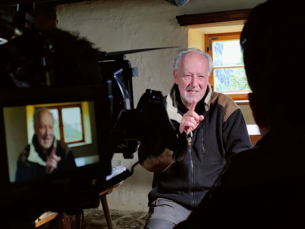 A man is sitting in front of a camera and giving a thumbs up.