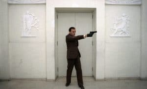 A man in a suit pointing a gun at a door.