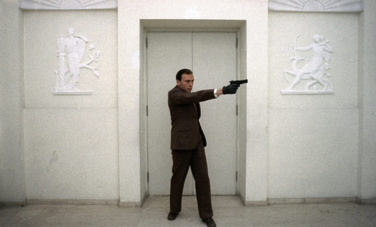 A man in a suit pointing a gun at a door.