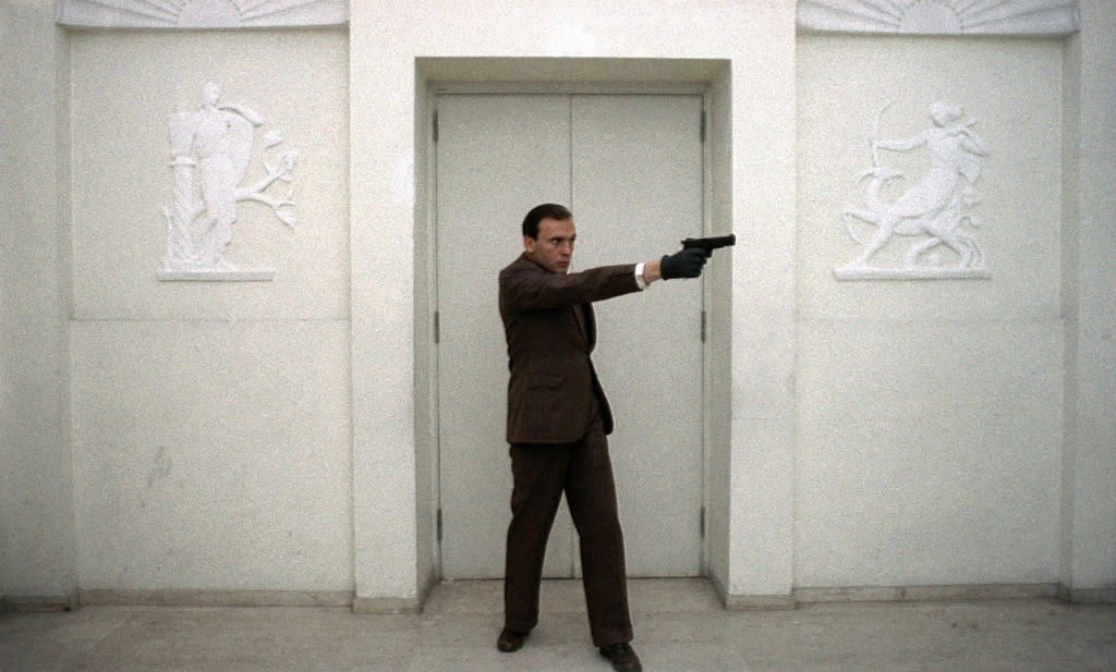 A man in a suit pointing a gun at a door.