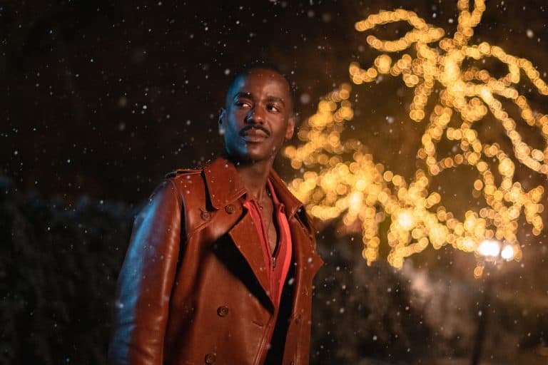 A man in a brown jacket standing in front of a christmas tree.