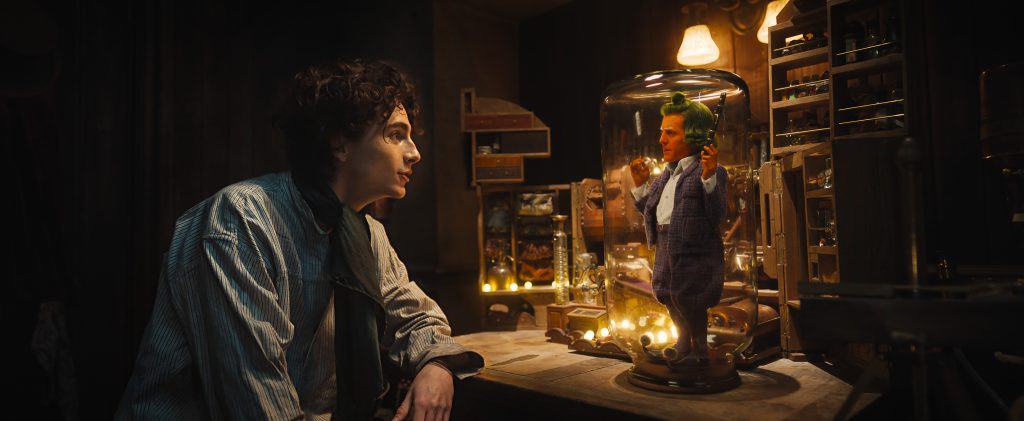 A man looking at a doll in a glass jar.