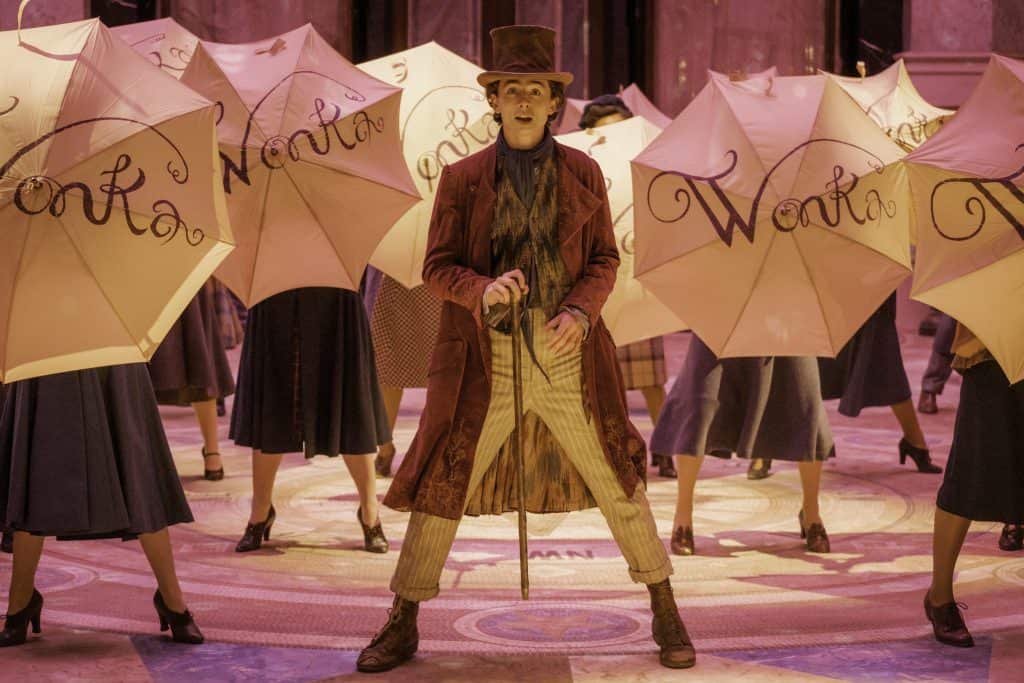 A man in a top hat holding umbrellas in front of a group of dancers.
