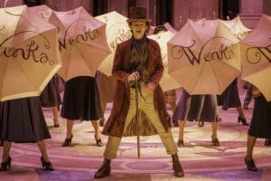 A man in a top hat holding umbrellas in front of a group of dancers.