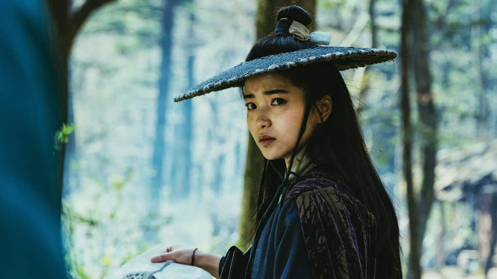 A woman in an asian hat is standing in the woods.