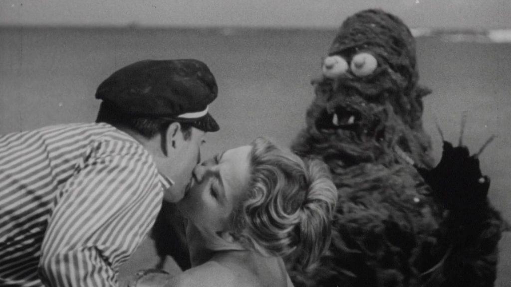 A man kisses a woman next to a giant monster.