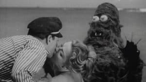A man kisses a woman next to a giant monster.