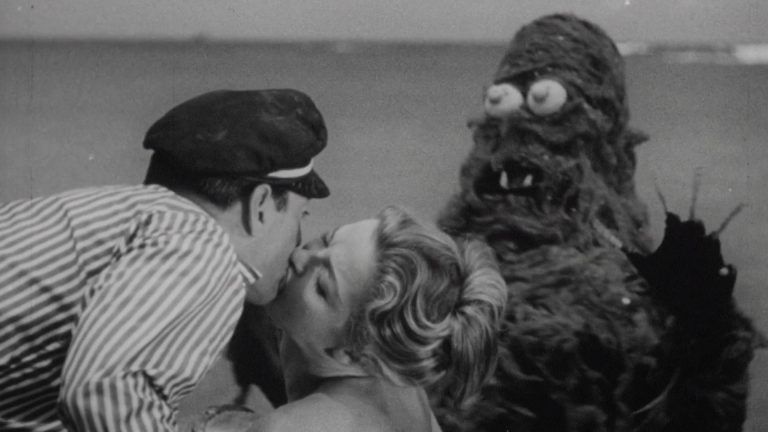 ‘The Devil’s Partner’ & ‘Creature From The Haunted Sea’ Blu-Ray Review – Two Schlocky Productions From Roger Corman A man kisses a woman next to a giant monster.
