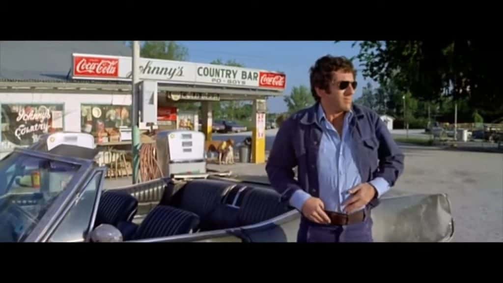 A man standing next to a car in front of a gas station.