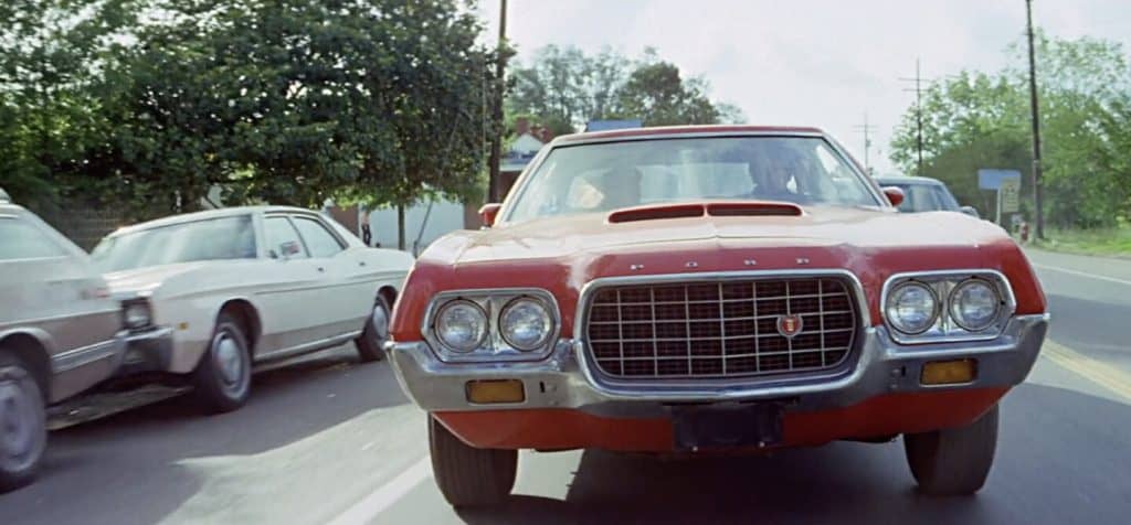 A red car driving down a street with other cars in the background.